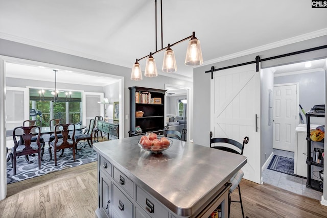 kitchen with a barn door, gray cabinetry, crown molding, light hardwood / wood-style flooring, and decorative light fixtures