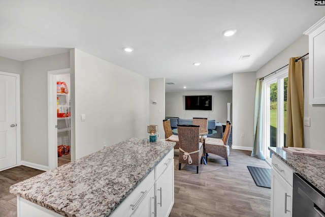 kitchen with a kitchen island, white cabinetry, dishwasher, light stone countertops, and light hardwood / wood-style floors