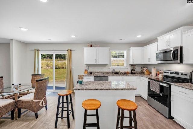 kitchen with plenty of natural light, appliances with stainless steel finishes, light stone countertops, and light wood-type flooring