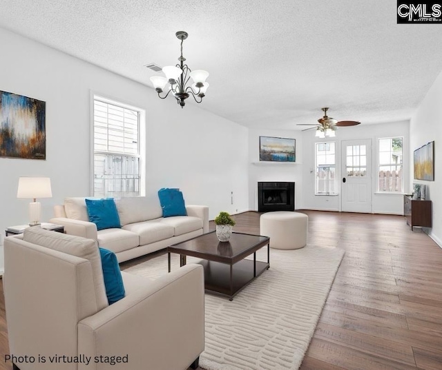 living room featuring ceiling fan with notable chandelier, wood-type flooring, and a textured ceiling