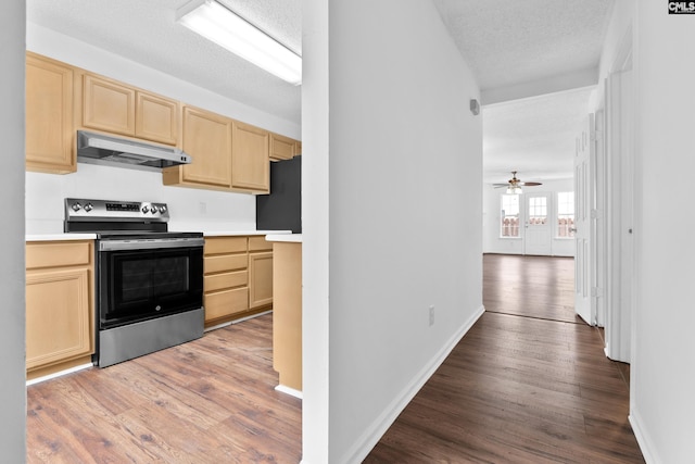 kitchen with stainless steel electric range oven, a textured ceiling, black fridge, light brown cabinetry, and light wood-type flooring