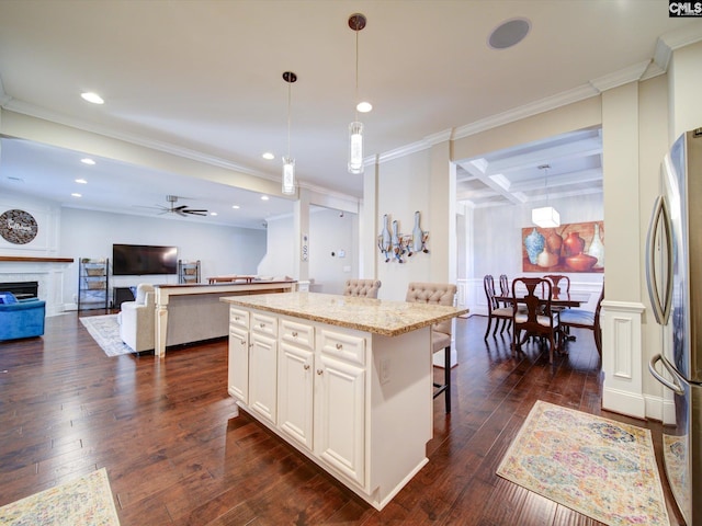 kitchen with a kitchen island, a kitchen bar, stainless steel refrigerator, and decorative light fixtures