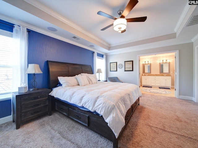 carpeted bedroom featuring a raised ceiling, ornamental molding, ensuite bath, and ceiling fan