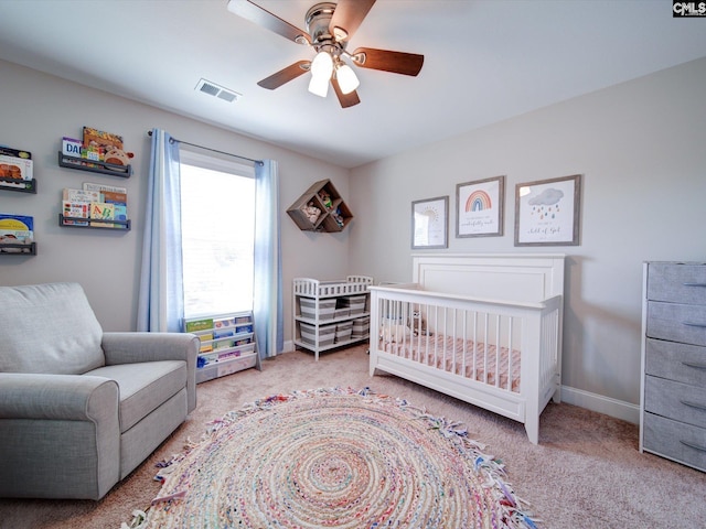 carpeted bedroom with ceiling fan and a crib