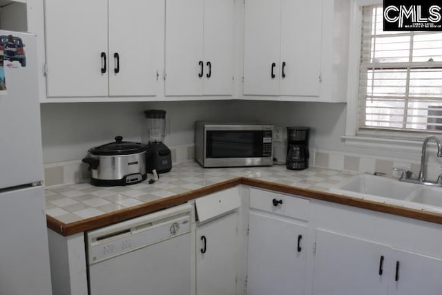 kitchen with tile counters, white cabinetry, sink, and white appliances