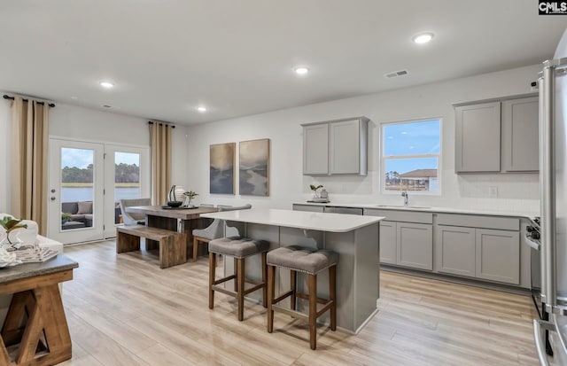 kitchen featuring gray cabinetry, a center island, a kitchen breakfast bar, light hardwood / wood-style floors, and decorative backsplash