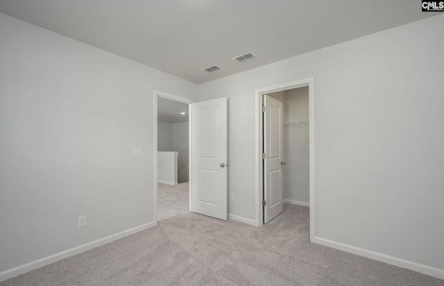 unfurnished bedroom with a walk in closet, a closet, and light colored carpet