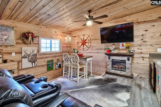 living room with wood walls, ceiling fan, hardwood / wood-style floors, and a stone fireplace