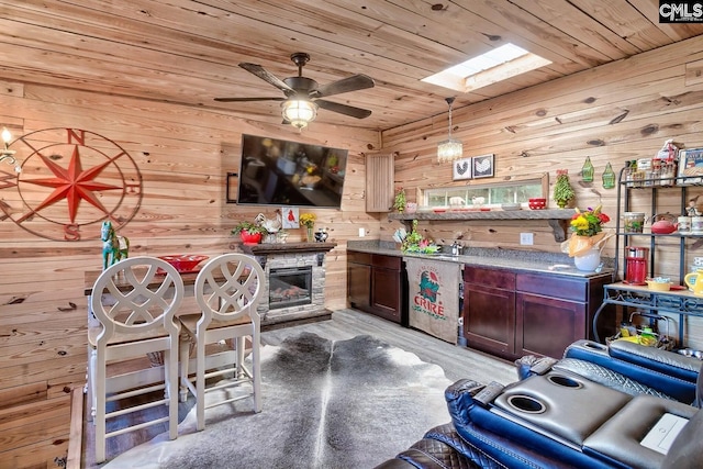 kitchen featuring ceiling fan, a skylight, hanging light fixtures, wood walls, and light hardwood / wood-style floors