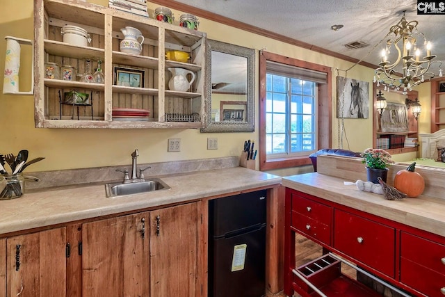 kitchen with black fridge, ornamental molding, sink, a textured ceiling, and a notable chandelier