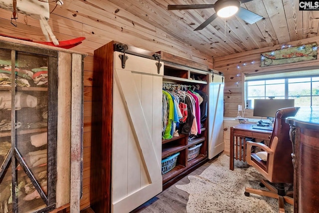 office area featuring ceiling fan, wood walls, hardwood / wood-style floors, wooden ceiling, and a barn door