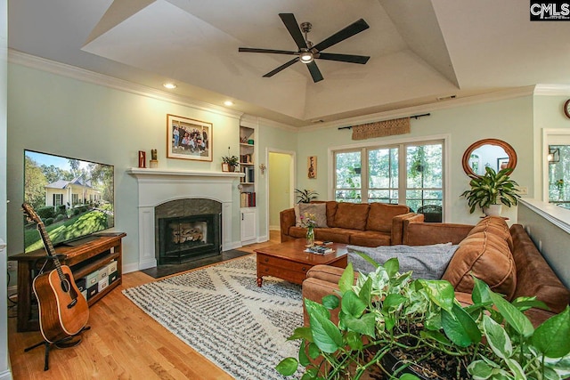 living room with ceiling fan, light wood-type flooring, ornamental molding, and a tray ceiling