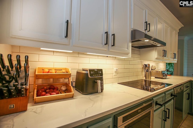 kitchen featuring green cabinetry, light stone counters, decorative backsplash, black appliances, and white cabinetry