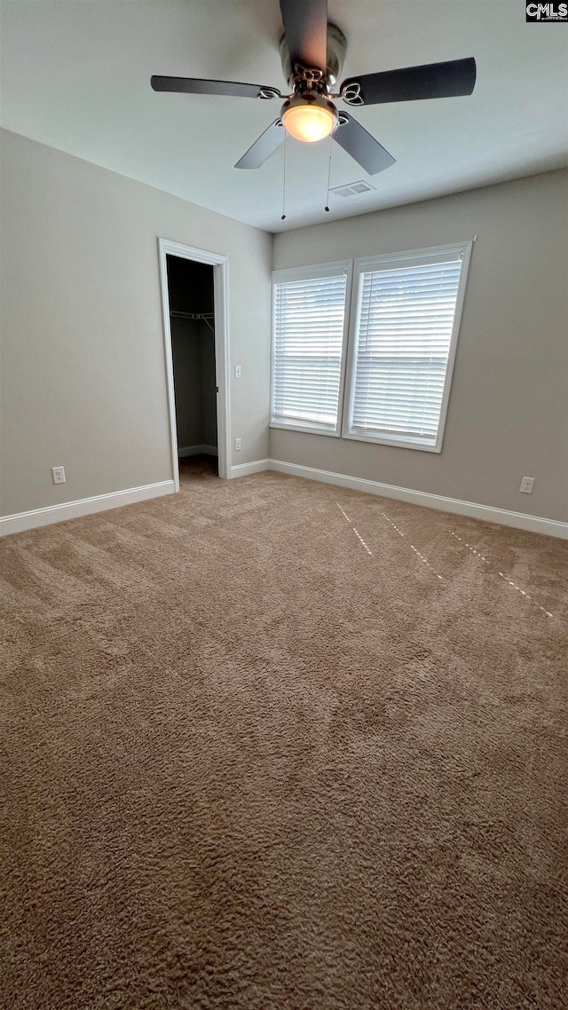 unfurnished bedroom featuring carpet floors, a closet, a walk in closet, and ceiling fan