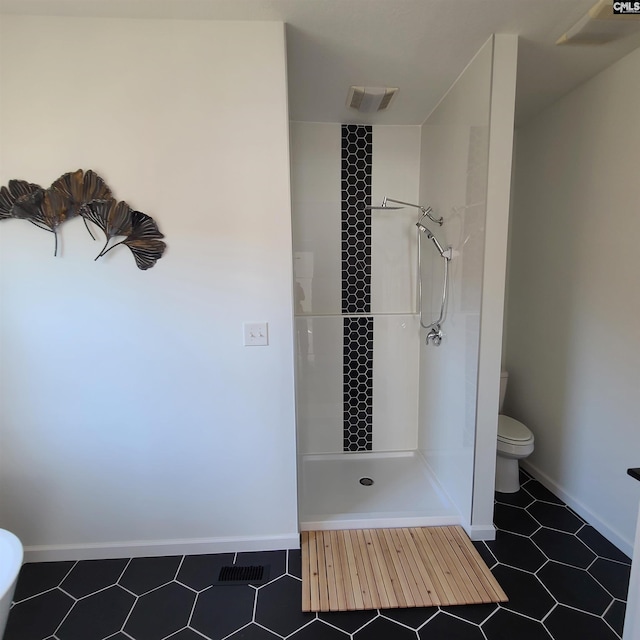 bathroom with a tile shower, toilet, and tile patterned floors