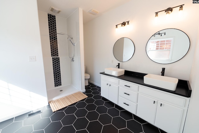 bathroom with vanity, a tile shower, toilet, and tile patterned flooring