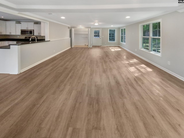 unfurnished living room with ornamental molding, sink, and light wood-type flooring