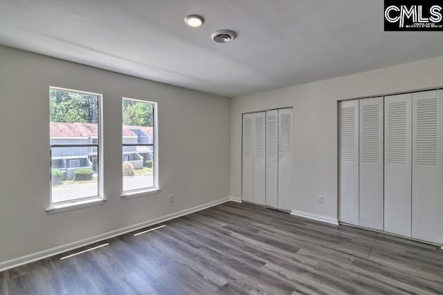 unfurnished bedroom featuring multiple closets and dark hardwood / wood-style flooring