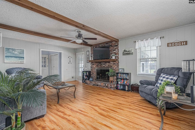 living room featuring ceiling fan, a fireplace, beamed ceiling, and wood-type flooring