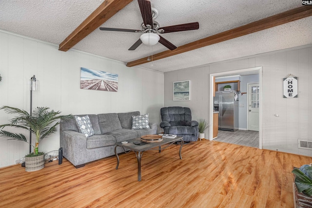 living room with beam ceiling, light wood-type flooring, a textured ceiling, and ceiling fan