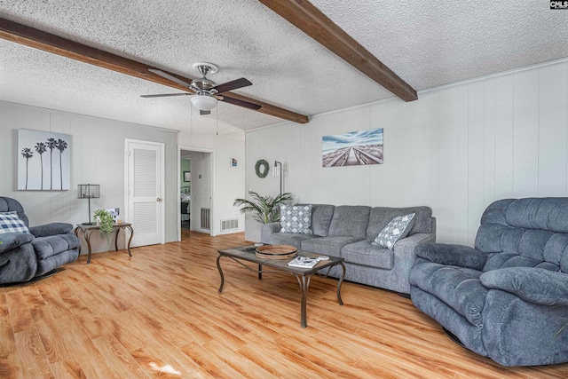 living room with beamed ceiling, ceiling fan, light hardwood / wood-style floors, and a textured ceiling