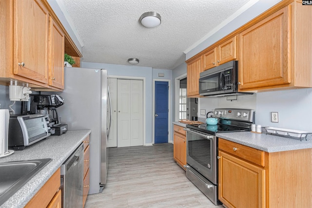 kitchen with a textured ceiling, sink, light wood-type flooring, and stainless steel appliances