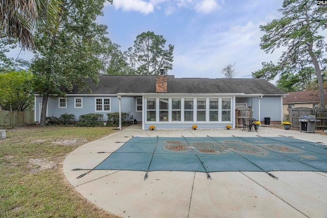 rear view of property featuring a patio area, a sunroom, a yard, and a covered pool