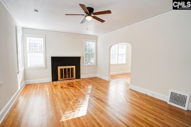 unfurnished living room featuring hardwood / wood-style floors, crown molding, a brick fireplace, a textured ceiling, and ceiling fan