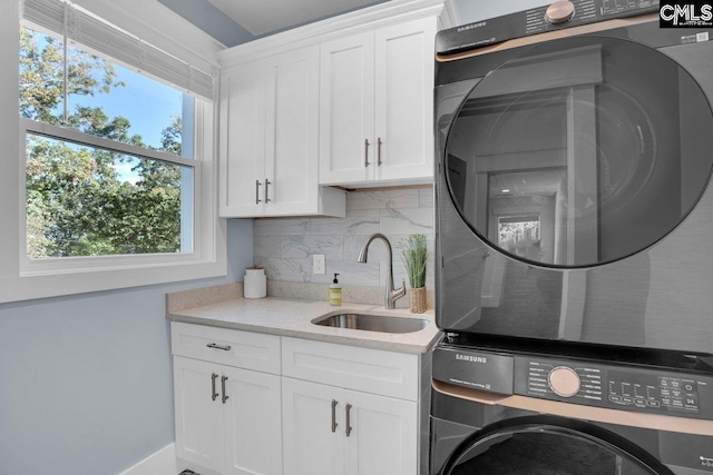 clothes washing area with sink, stacked washer / dryer, a healthy amount of sunlight, and cabinets