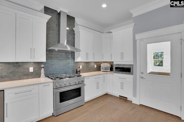 kitchen featuring wall chimney range hood, stainless steel appliances, crown molding, white cabinets, and light hardwood / wood-style floors