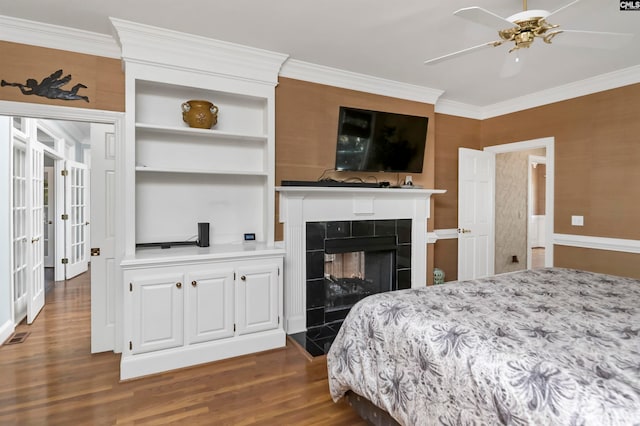 bedroom featuring ceiling fan, ornamental molding, dark hardwood / wood-style flooring, and a tile fireplace