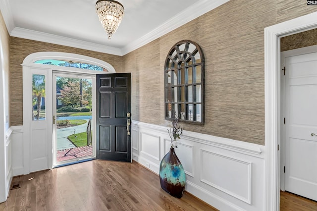 entryway with a notable chandelier, wood-type flooring, and ornamental molding