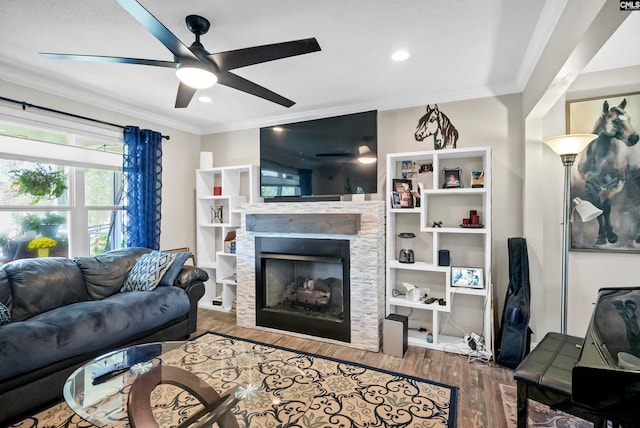 living room with crown molding, wood-type flooring, a fireplace, and ceiling fan