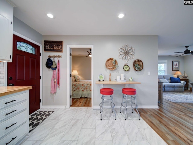 interior space with white cabinets, ceiling fan, a kitchen breakfast bar, light hardwood / wood-style flooring, and butcher block countertops