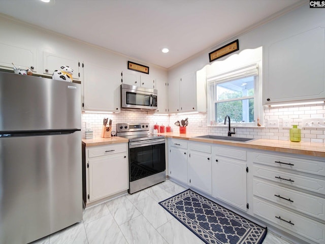 kitchen featuring decorative backsplash, stainless steel appliances, crown molding, sink, and white cabinets