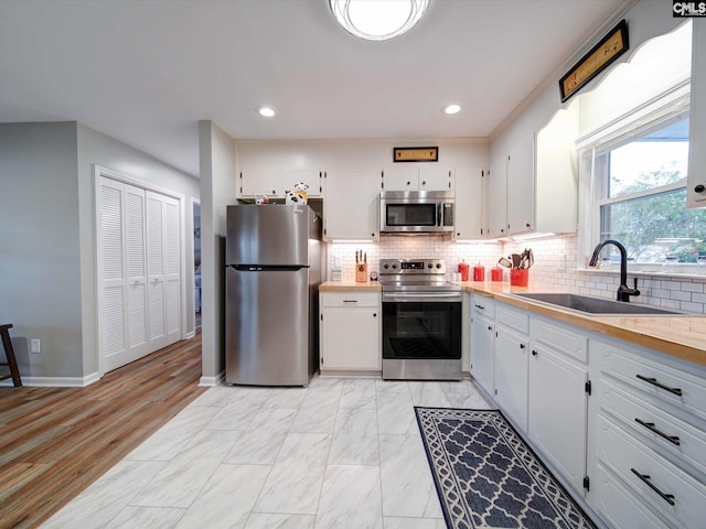 kitchen with sink, backsplash, white cabinetry, light hardwood / wood-style floors, and stainless steel appliances