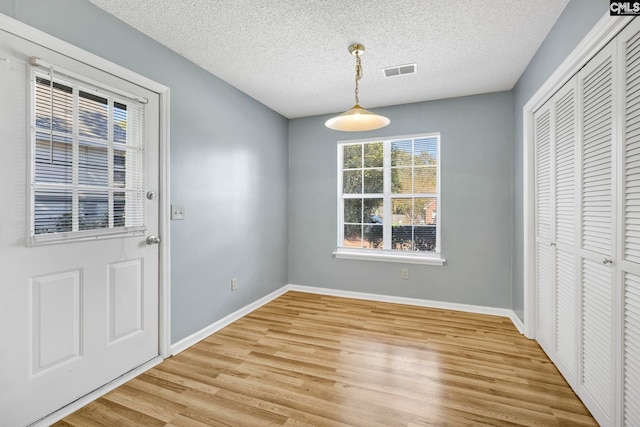 unfurnished dining area featuring a textured ceiling and light wood-type flooring