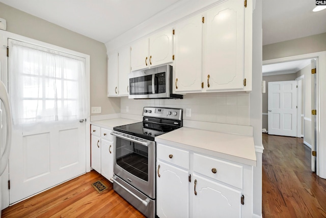 kitchen with backsplash, appliances with stainless steel finishes, light wood-type flooring, and white cabinets