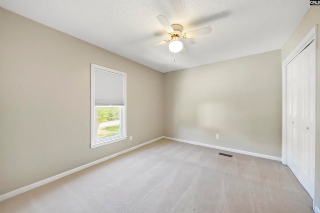 unfurnished bedroom featuring light carpet, a textured ceiling, a closet, and ceiling fan