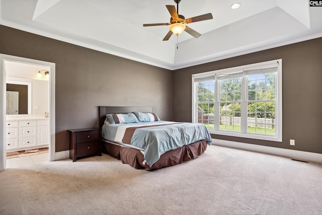 carpeted bedroom featuring ceiling fan, a tray ceiling, and ensuite bath