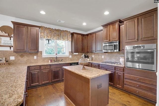 kitchen with appliances with stainless steel finishes, dark wood-type flooring, light stone countertops, a kitchen island, and sink