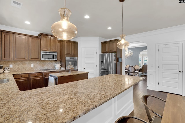 kitchen with light stone counters, decorative light fixtures, stainless steel appliances, and a breakfast bar area