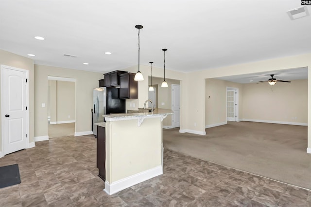 kitchen featuring light carpet, stainless steel fridge, a kitchen bar, decorative light fixtures, and light stone counters