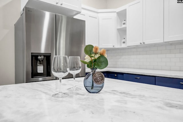 interior details featuring light stone counters, stainless steel fridge, white cabinets, and decorative backsplash