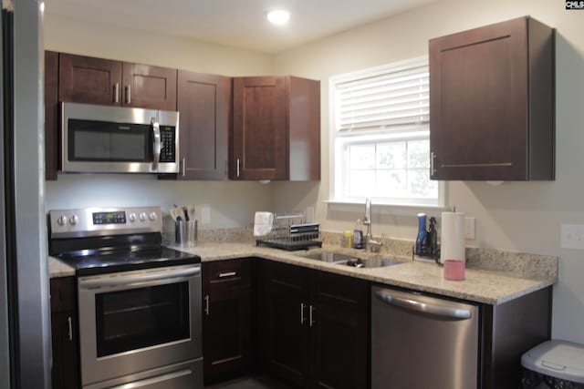 kitchen with sink, light stone countertops, dark brown cabinets, and stainless steel appliances