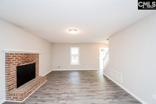 unfurnished living room with hardwood / wood-style flooring and a brick fireplace