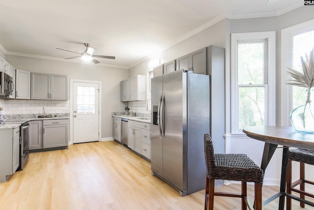 kitchen featuring appliances with stainless steel finishes, light wood-type flooring, decorative backsplash, gray cabinets, and ornamental molding