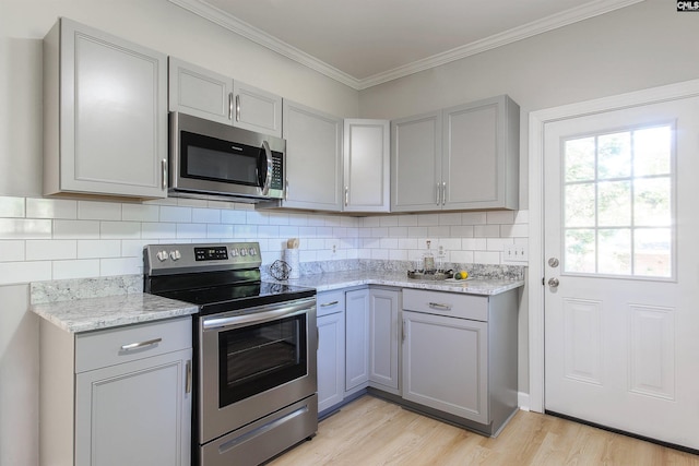 kitchen with gray cabinetry, light stone counters, stainless steel appliances, and light wood-type flooring