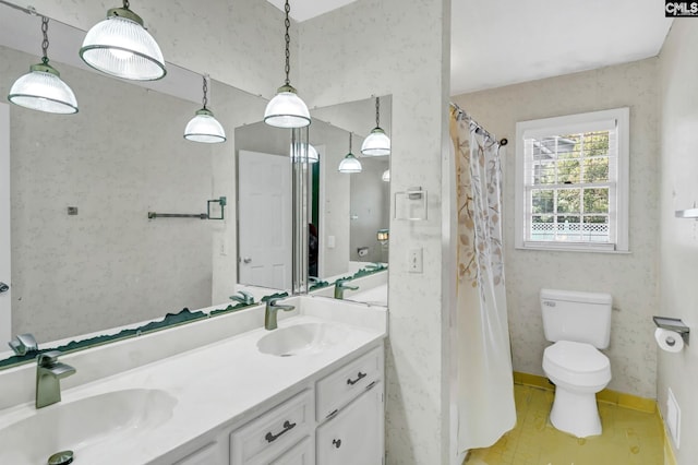 bathroom featuring double vanity, toilet, baseboards, and a sink