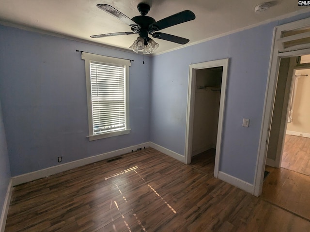 unfurnished bedroom with a walk in closet, a closet, ceiling fan, ornamental molding, and dark hardwood / wood-style floors